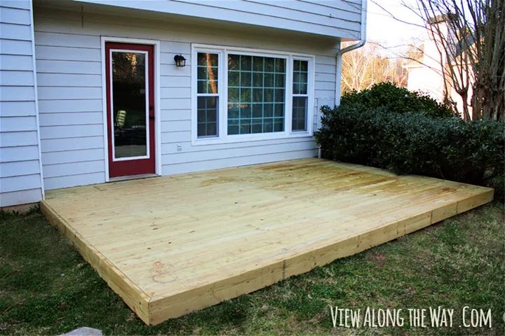 a wooden deck in front of a white house with red door and window on the side