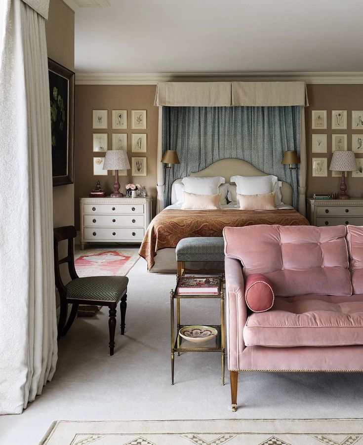 a pink couch sitting in front of a bed next to a chair and table with two lamps on top of it