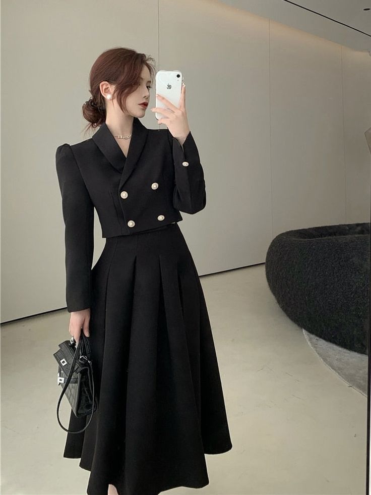 a woman taking a selfie in front of a mirror wearing a black coat and dress