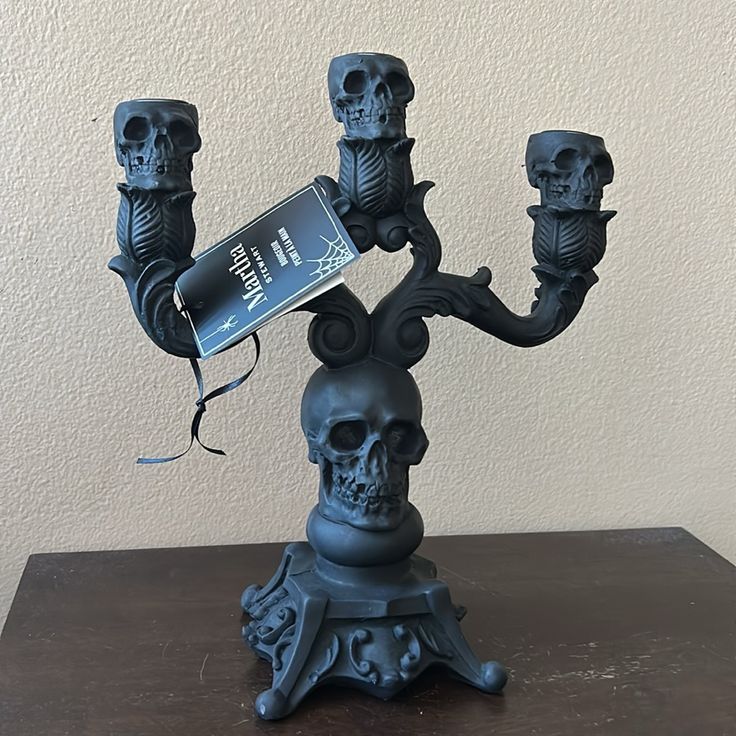 a black candle holder with three candles and a skull on the top, sitting on a table