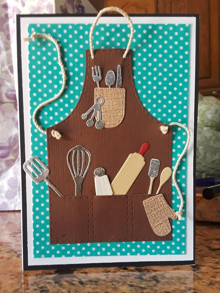 a handmade card with an apron and kitchen utensils on it, sitting on a table