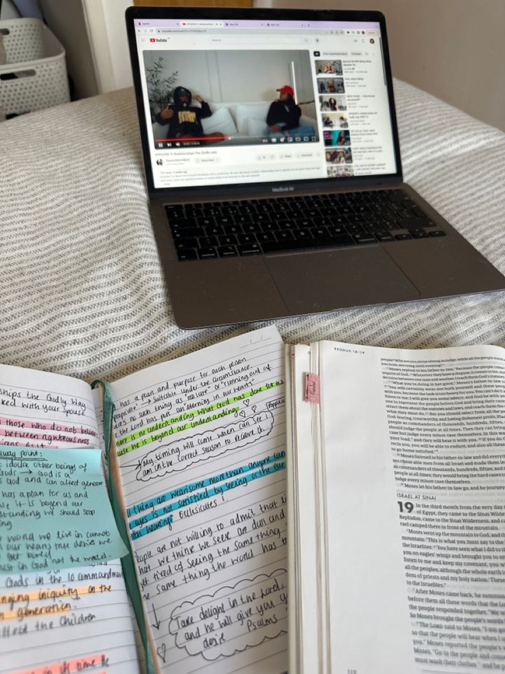 a laptop computer sitting on top of a bed next to an open book and notebook