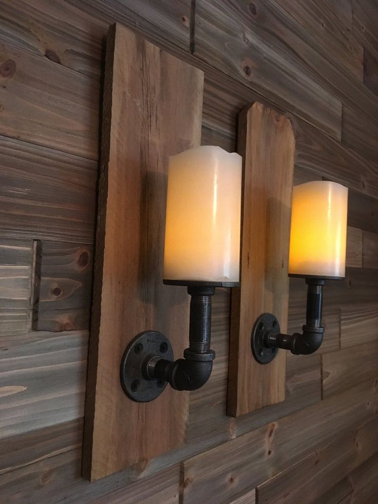 two candles are lit on the wall next to wood planks and sconces