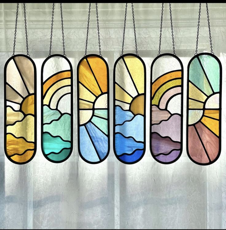 four stained glass windows hanging from chains in front of a window with the sun shining through them