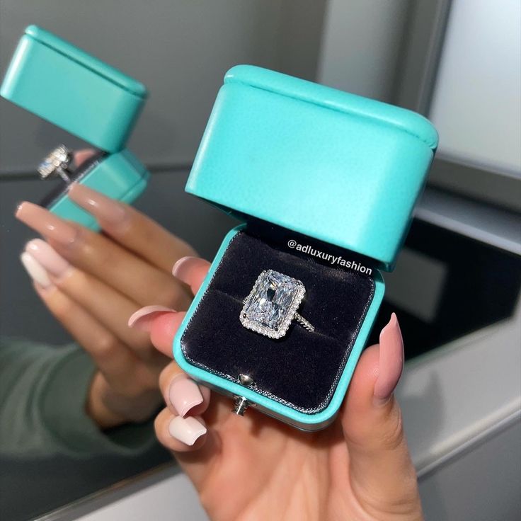 a woman holding an engagement ring in a blue box with the lid open to show it's inside