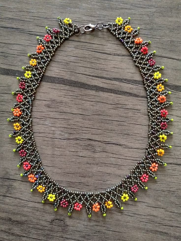 a beaded necklace on a wooden surface with beads in the shape of flowers and leaves