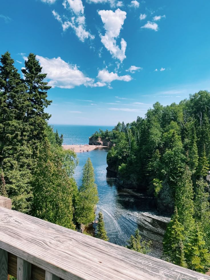 a wooden deck overlooks the water and trees on a sunny day with blue skies