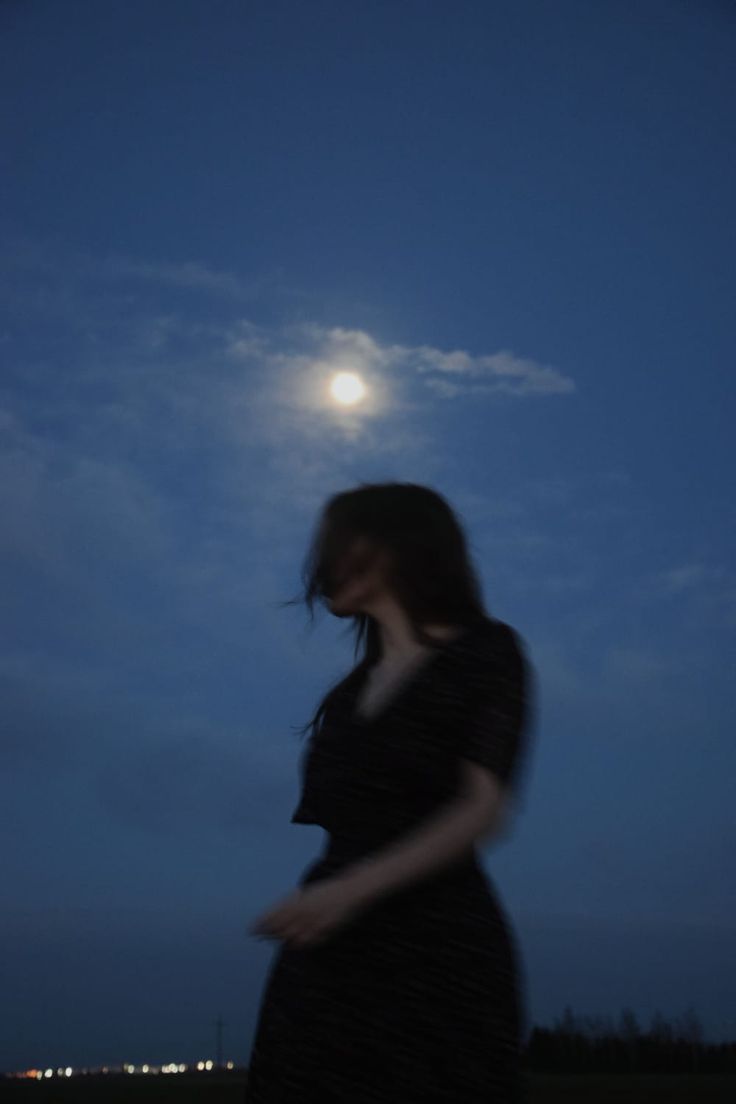 a woman standing in the grass at night with her hand on her hip, looking down