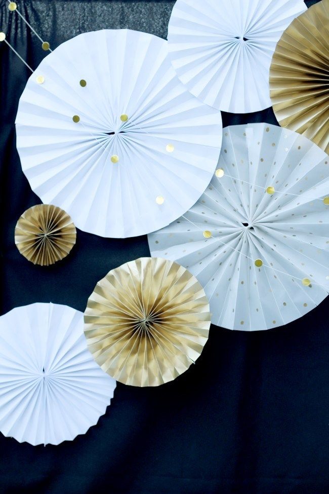 white and gold paper parasols hanging on a black backdrop with confetti