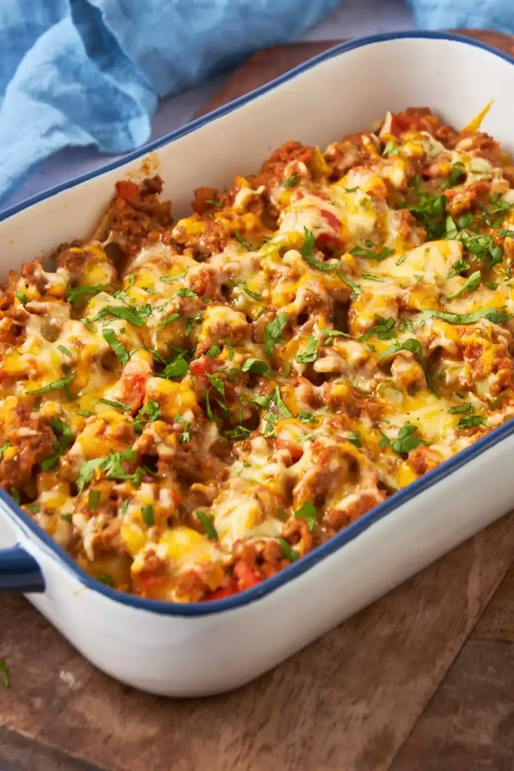 a casserole dish with meat and vegetables in it on a wooden table next to a blue towel