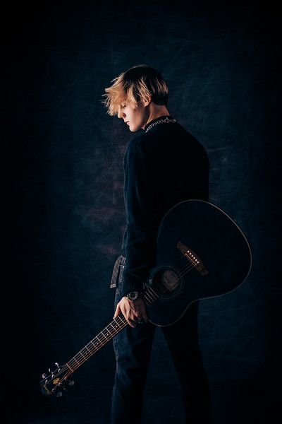 a young man holding an acoustic guitar in his hands and looking down at the ground