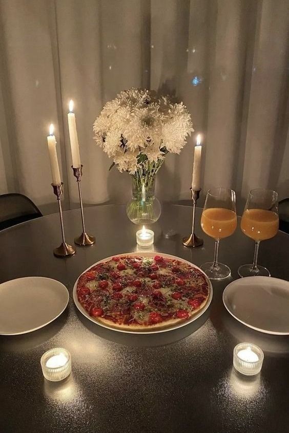 a table topped with a pizza next to two glasses of wine and plates filled with food