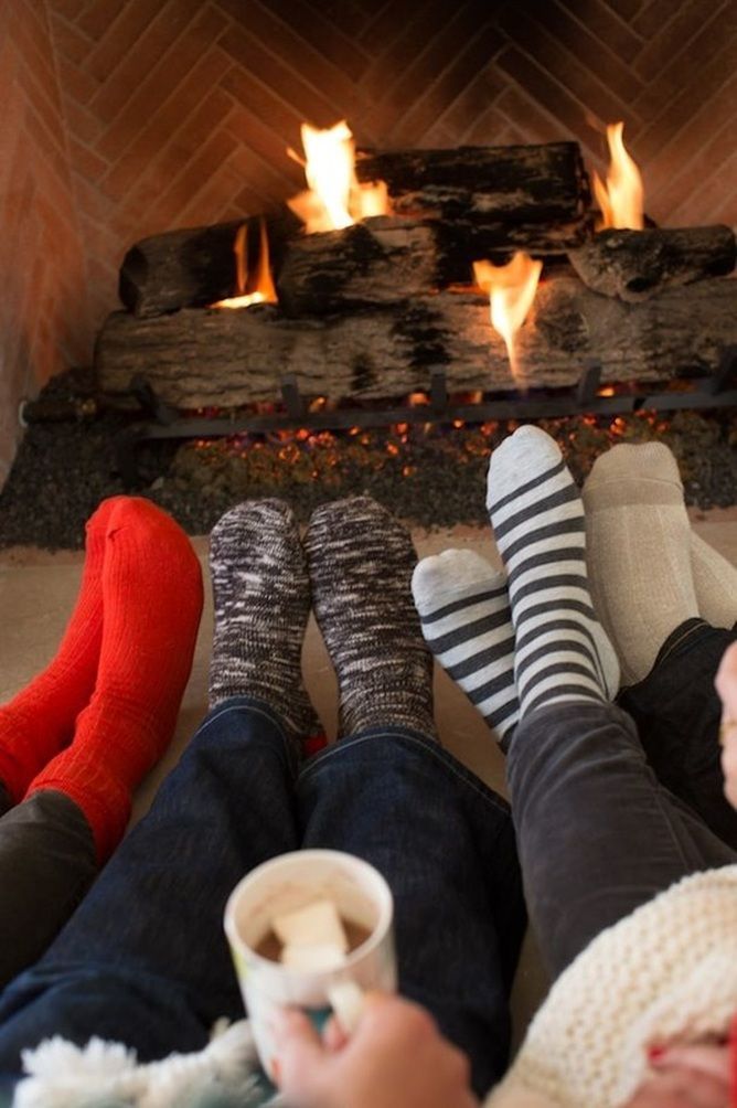 two people sitting in front of a fireplace with their feet up on the floor while holding coffee cups