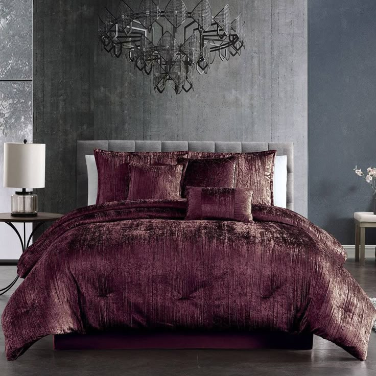 a bed with purple comforter and pillows in a room next to a chandelier