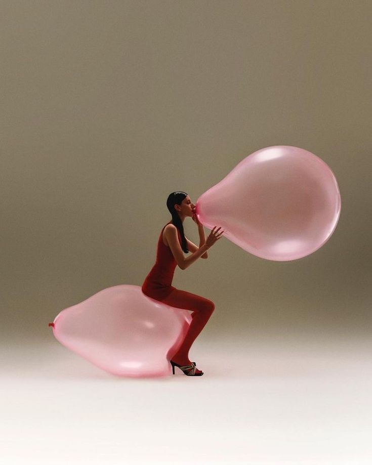 a woman in a red dress is holding two large pink balloons while standing on one leg