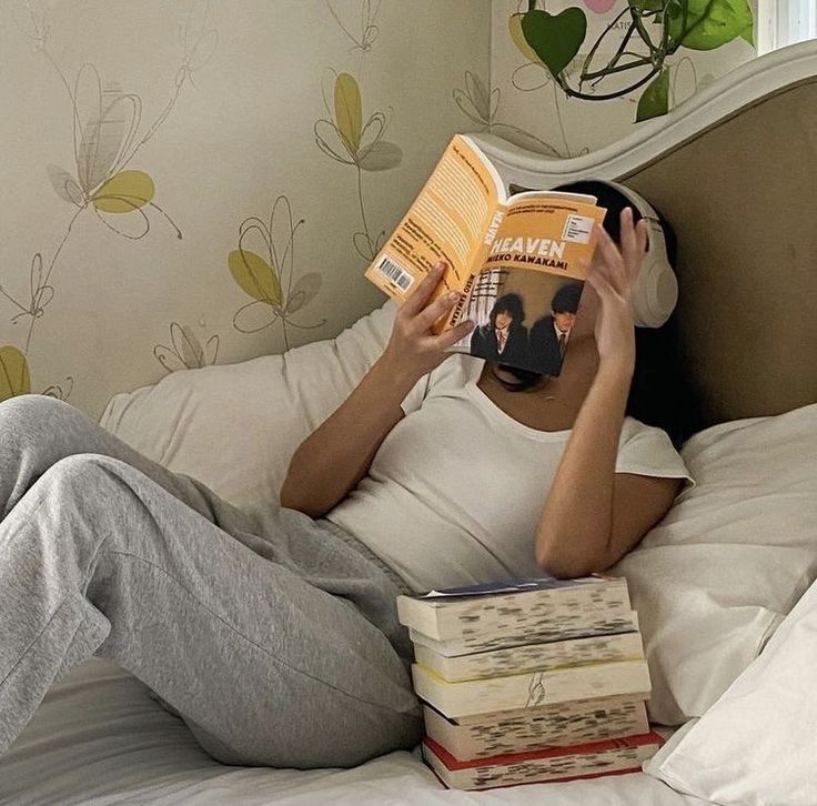 a person laying in bed reading a book with headphones on their ears and holding two books