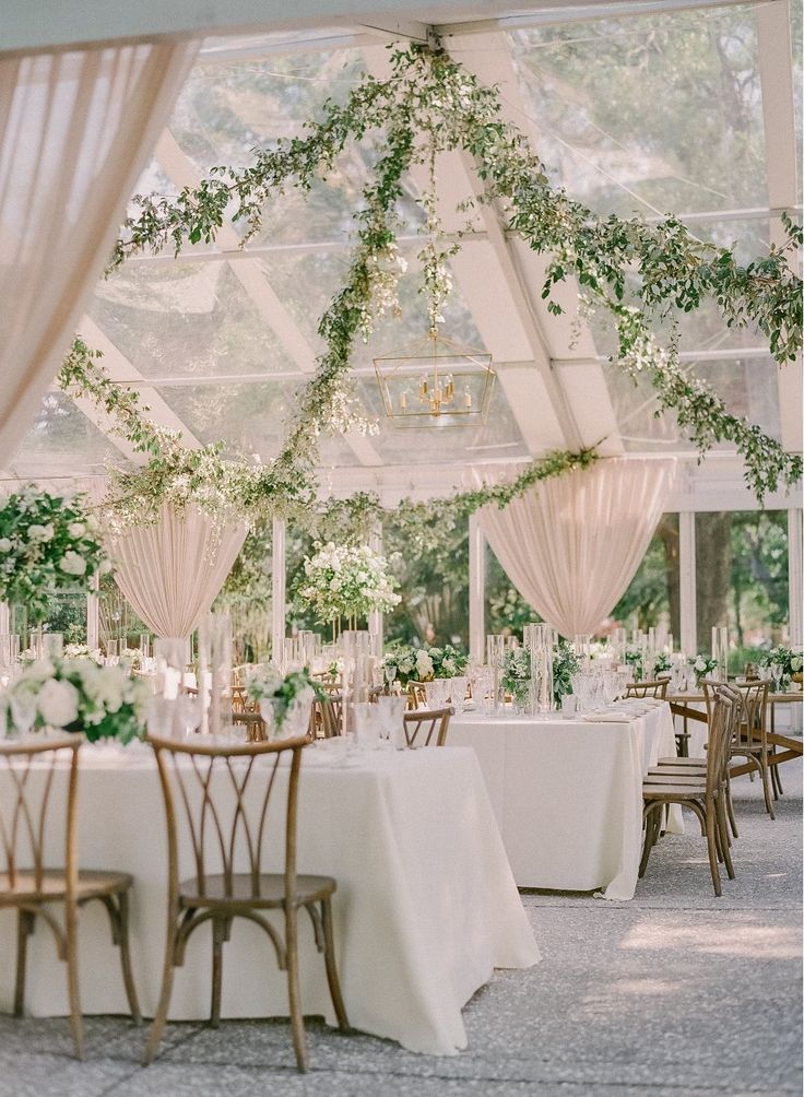 the tables are set with white linens and greenery on them for an elegant wedding reception