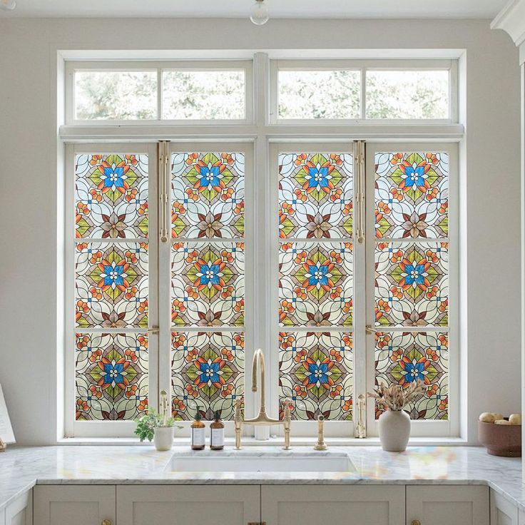 a kitchen window with colorful stained glass in the center and side panels on the windowsill