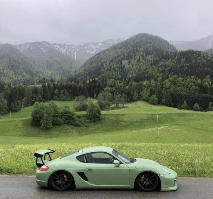 a green sports car parked on the side of a road in front of some mountains