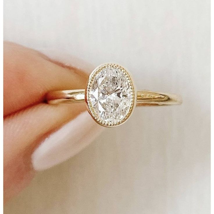 a woman's hand holding a yellow gold ring with a white diamond in the center