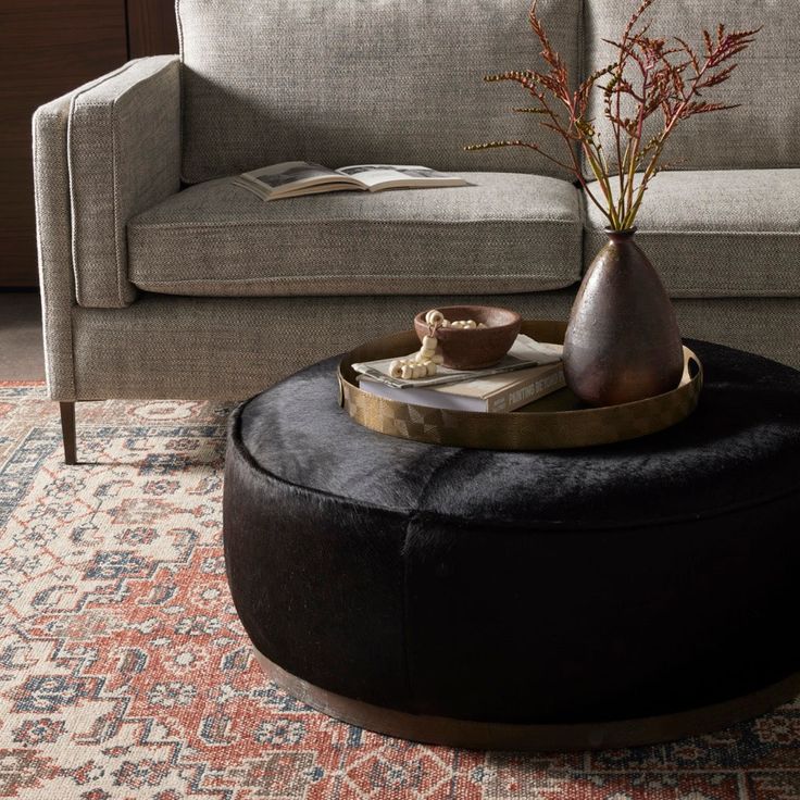 a living room with a couch, coffee table and vase on top of the ottoman