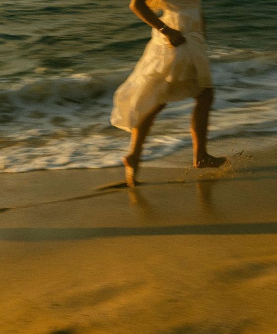 a woman in a white dress walking along the beach