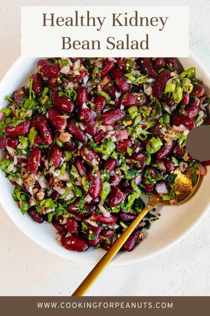 a white bowl filled with beans and other vegetables next to a spoon on top of a table