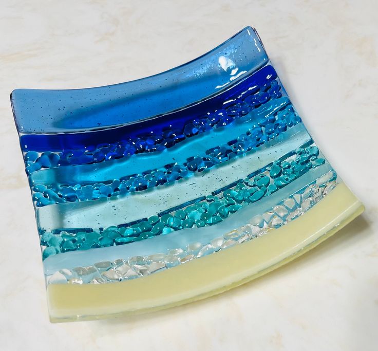 a blue and yellow glass dish with water droplets on it's sides, sitting on a white surface