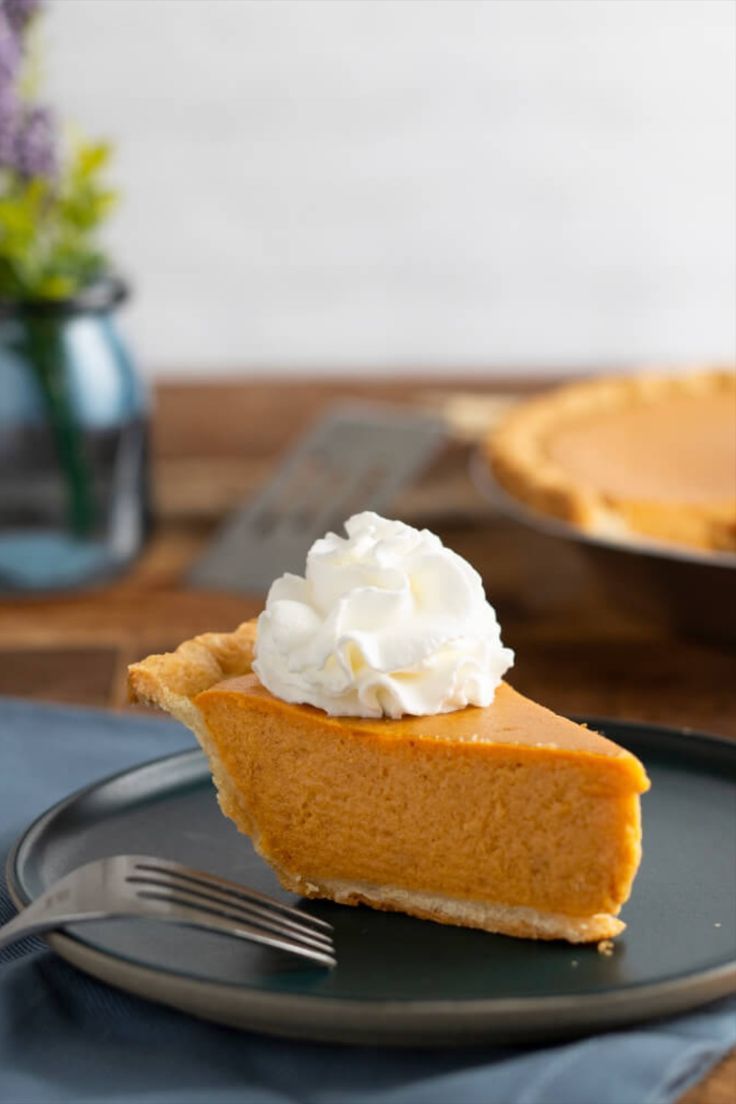 a slice of pumpkin pie on a black plate with a fork and blue napkin next to it