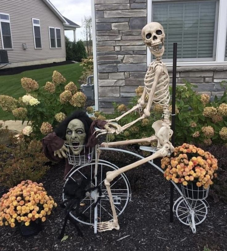 a skeleton on a bicycle with flowers in the front yard