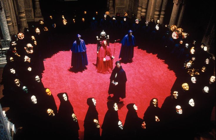 a group of people standing in front of a red circle surrounded by black heads and masks