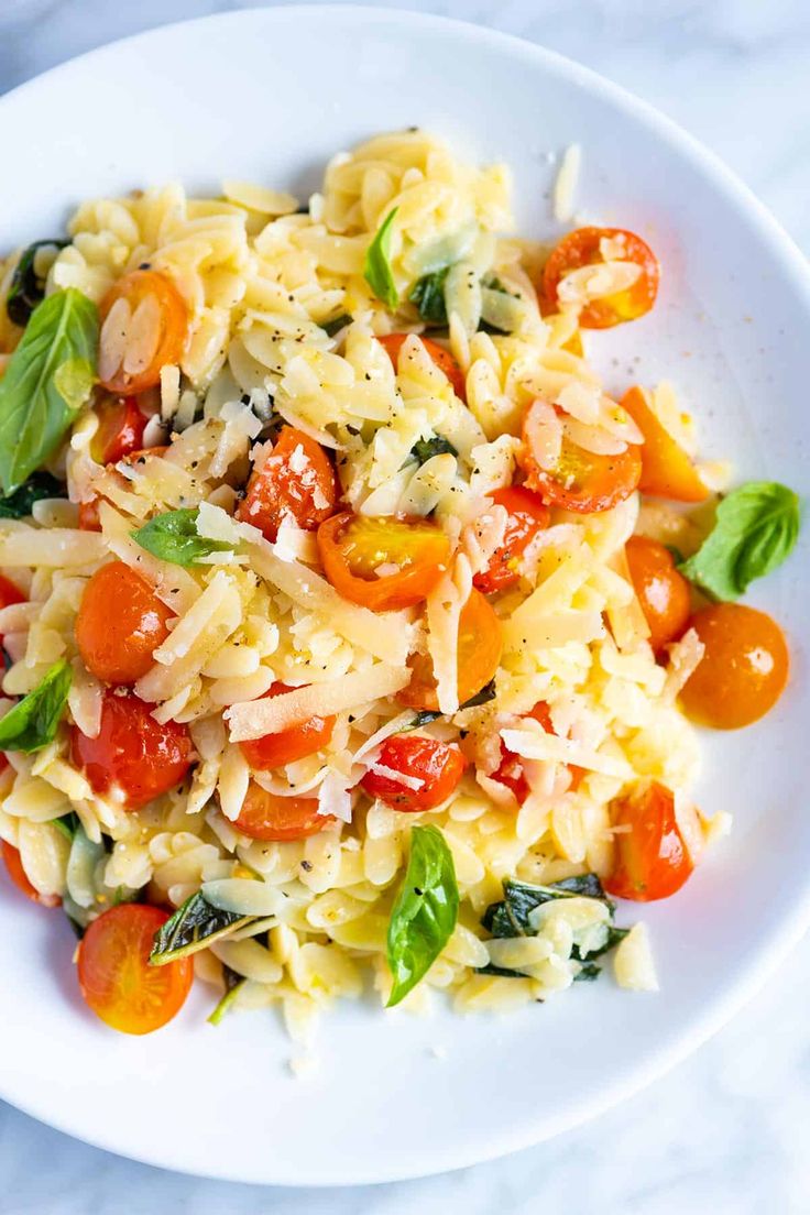 a white plate topped with pasta and veggies on top of a marble table