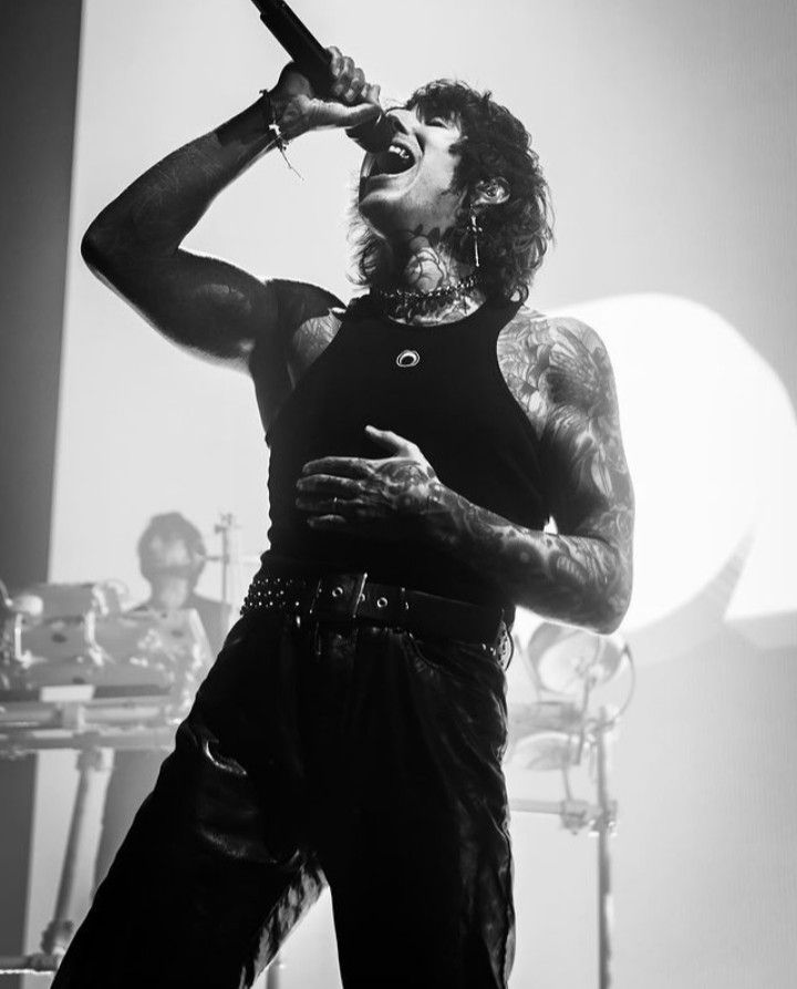 a man with long hair and piercings holding a microphone up to his mouth while standing in front of a stage