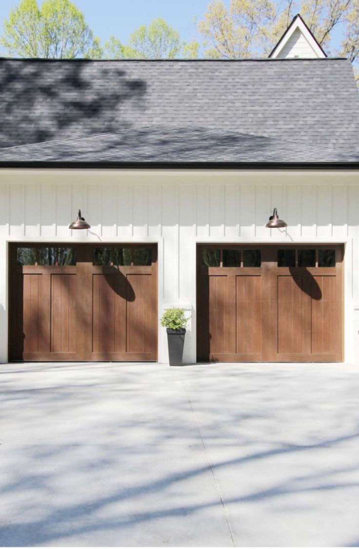 three brown garage doors are open in front of a white building with two planters