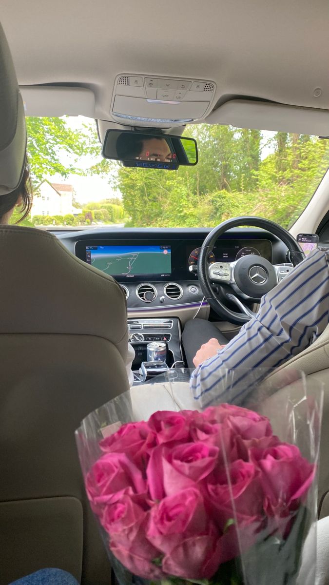 a bouquet of pink roses sits in the front seat of a car as a driver looks on