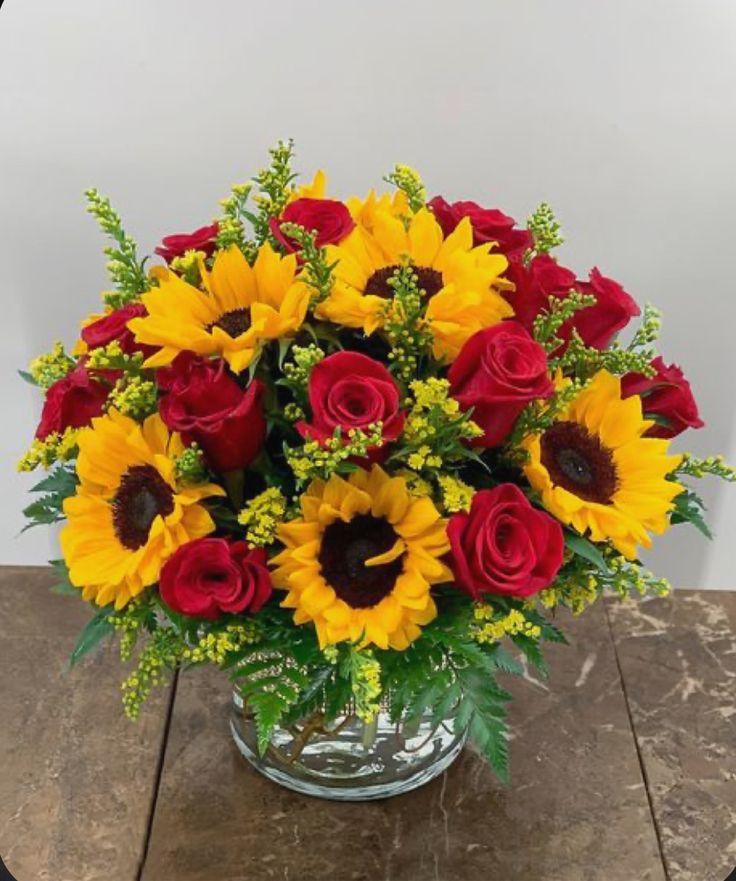 a vase filled with red roses and yellow sunflowers