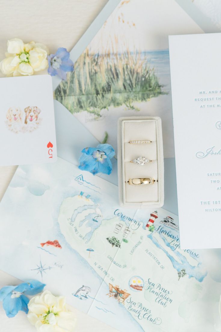 two wedding rings sitting on top of an open box next to some cards and flowers