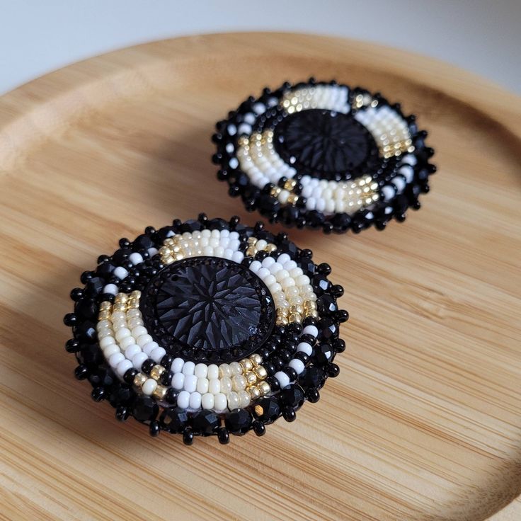 two black and white beaded earrings sitting on top of a wooden tray