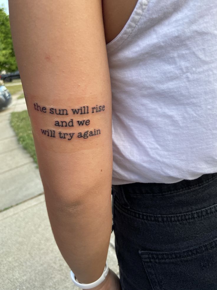 a person with a tattoo on their arm that says, the sun will rise and we will try again