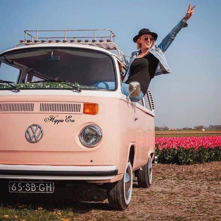 a woman standing on top of a pink vw bus in front of tulips