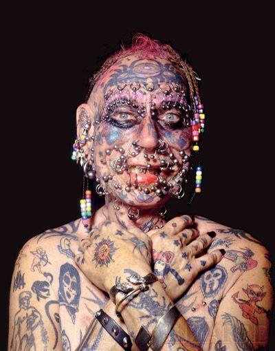 a woman with tattoos and piercings on her face is posing for the camera in front of a black background