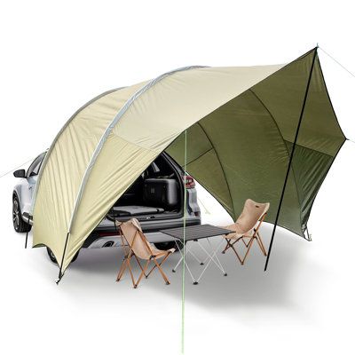 a tent attached to the back of a car with two chairs and a table underneath it