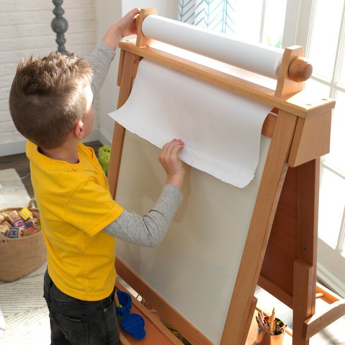 a little boy that is standing in front of a easel with some paper on it