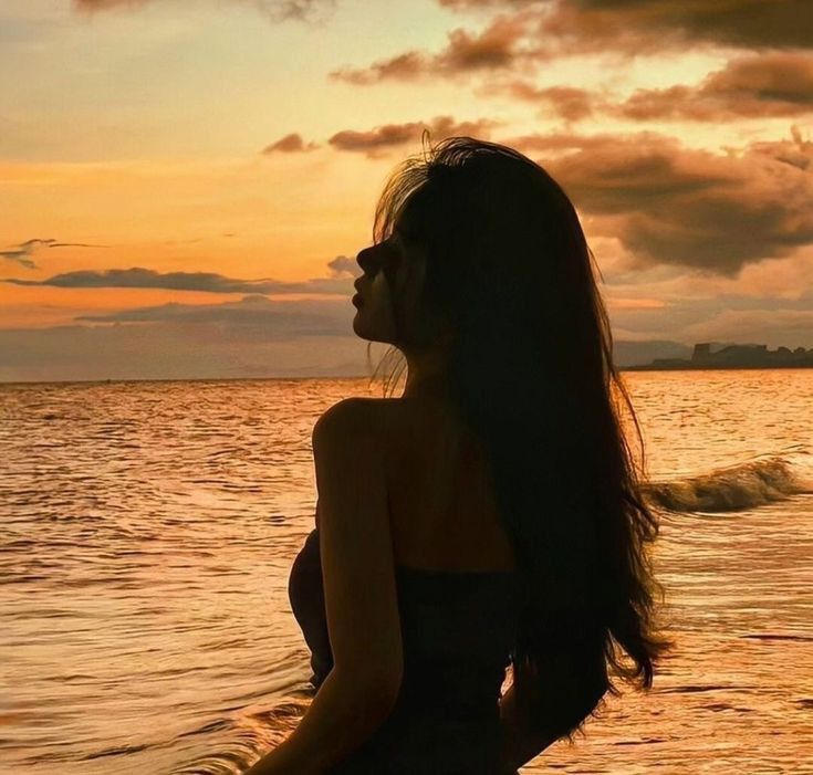 a woman standing in the water at sunset with her long hair blowing in the wind