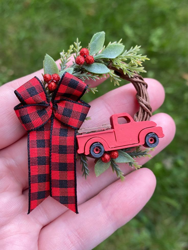 a hand holding a red and black christmas ornament with a truck on it