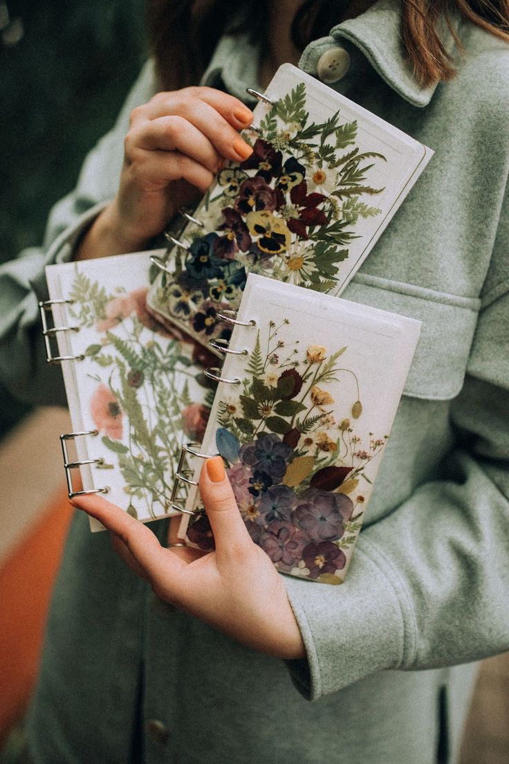 a woman holding three notebooks with flowers on them