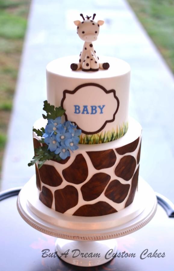 a giraffe themed baby shower cake with blue flowers on the bottom and a giraffe top