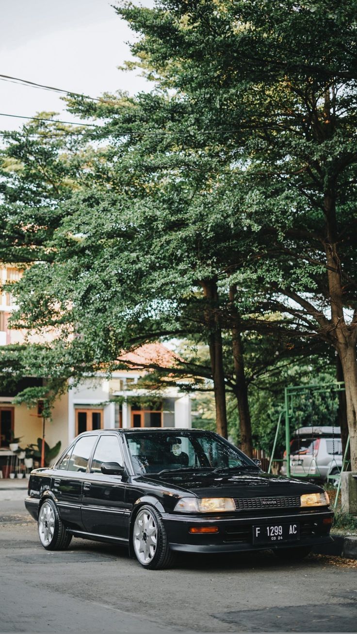 a black car is parked on the side of the road in front of some trees