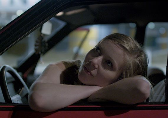 a woman sitting in the driver's seat of a red car with her arms crossed