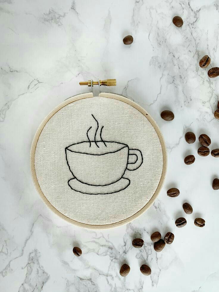 a cup of coffee on a table with coffee beans around it and the embroidery design